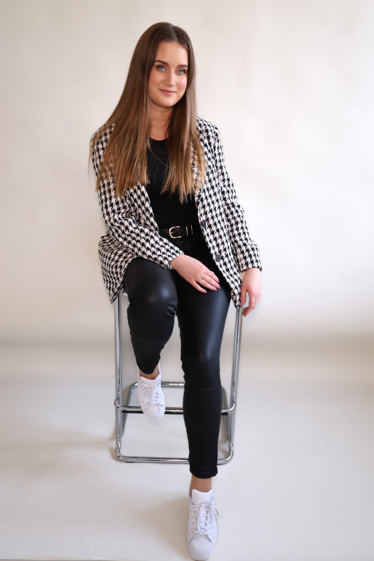 Wiktoria Pomorska siedząca na krześle, w marynarce w pepitkę, na jasnym studyjnym tle